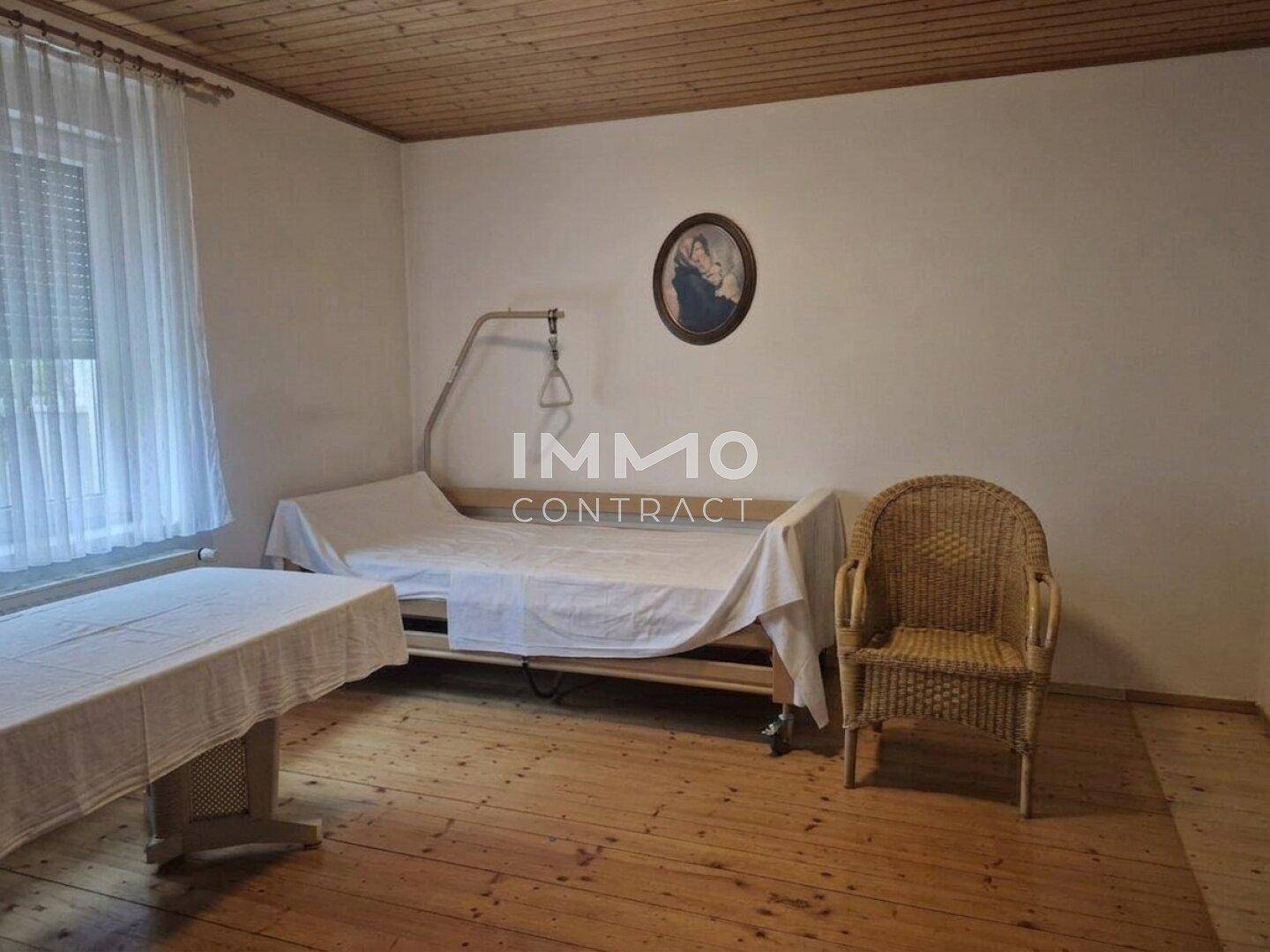 Schlafzimmer mit Holzdielenboden, Holzdecke und einem Einzelbett mit Pflegehilfe.