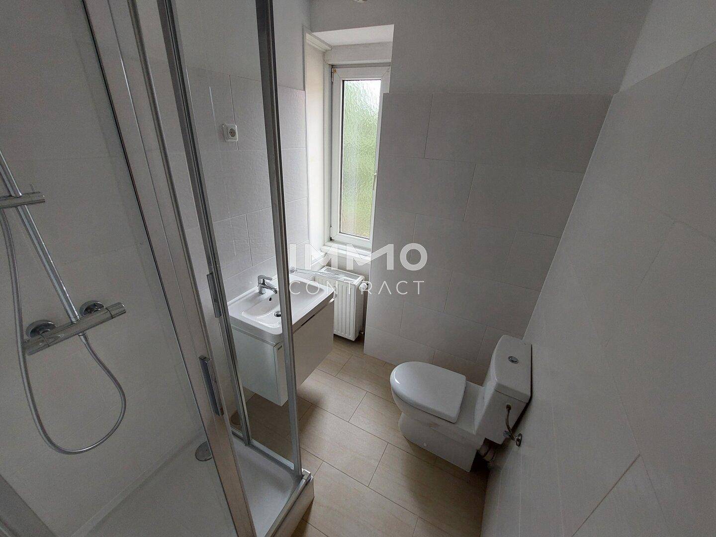 Modernes Badezimmer mit Duschkabine, WC, Waschbecken und Fenster.
