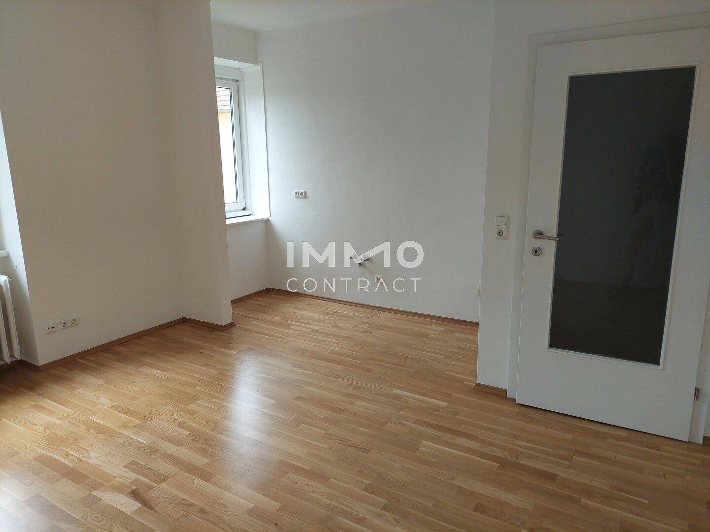 Helles Zimmer mit Holzboden, weiß gestrichenen Wänden und Fenster.
