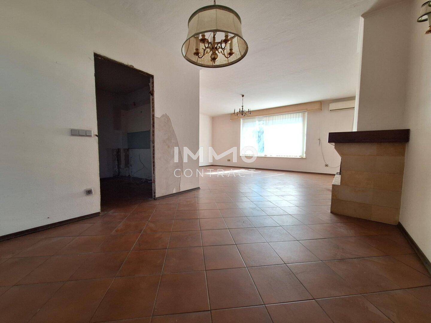 Geräumiges Wohnzimmer mit Fliesenboden und vorbereitetem Kaminbereich, bereit zur Renovierung.