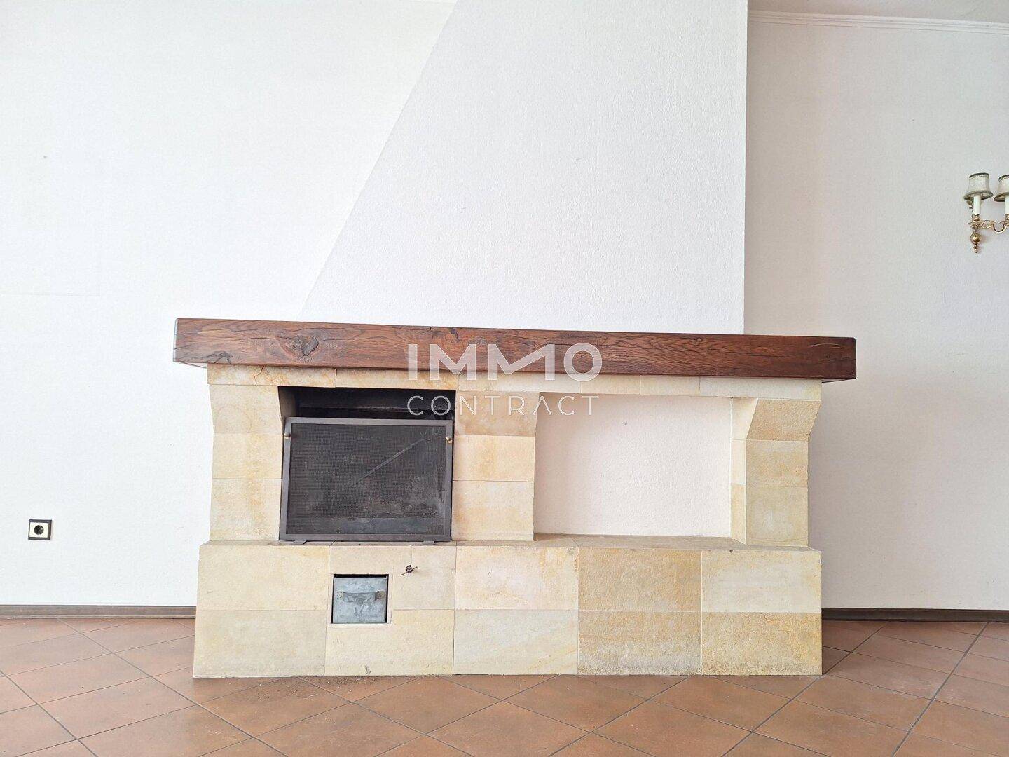 Detailansicht des gemauerten Kamins mit Holzbalken, ein zentrales Element im Wohnzimmer.