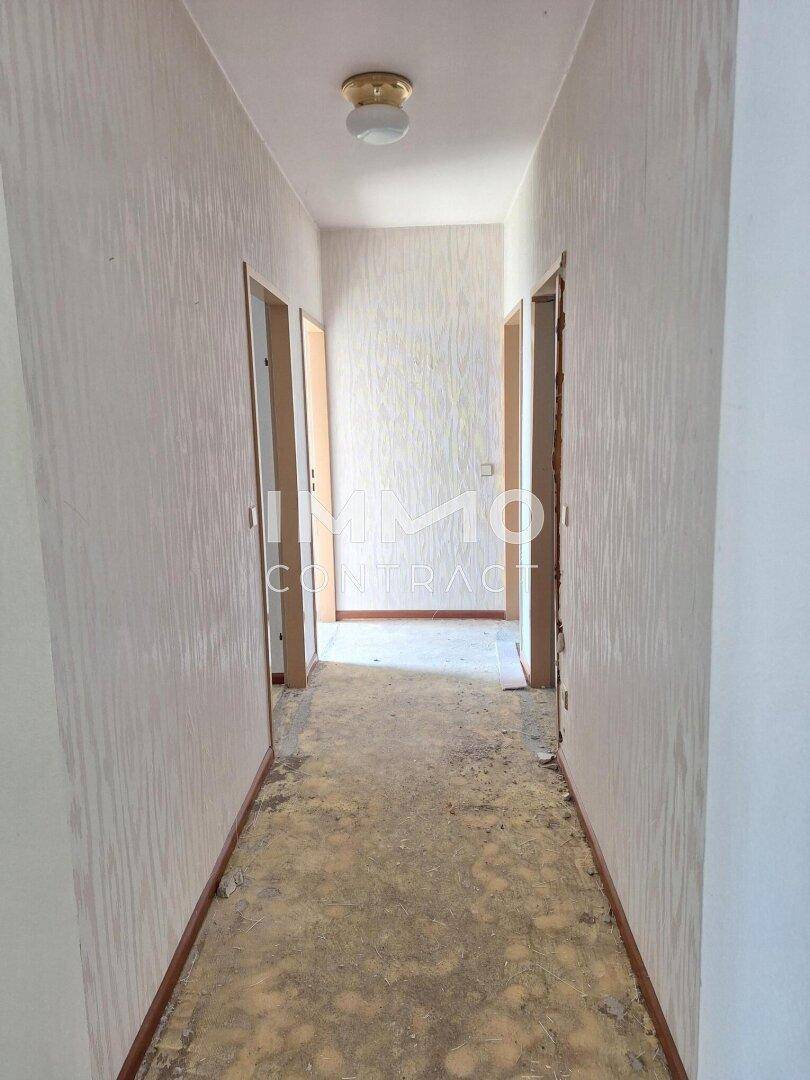 Langer Flur mit Tapetenresten und mehreren Türöffnungen, bietet Zugang zu verschiedenen Räumen.
