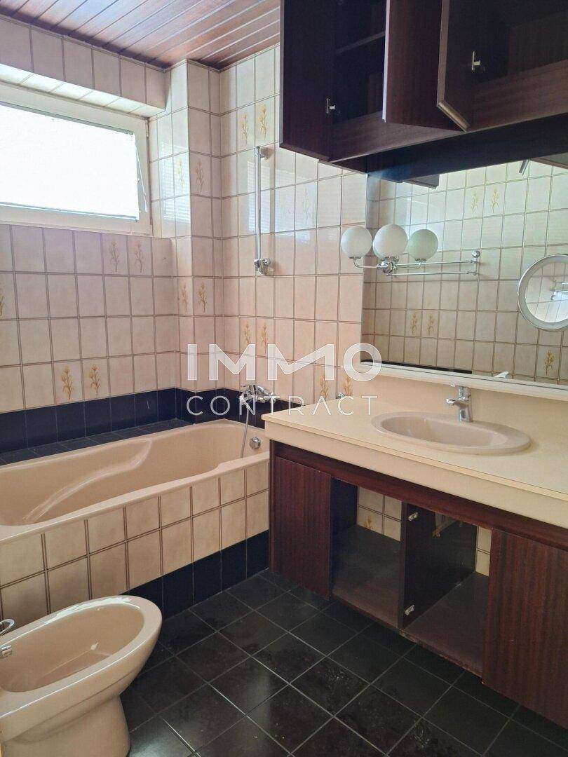 Badezimmer im Stil der 80er Jahre mit Badewanne, Bidet und Doppelwaschbecken, renovierungsbedürftig.