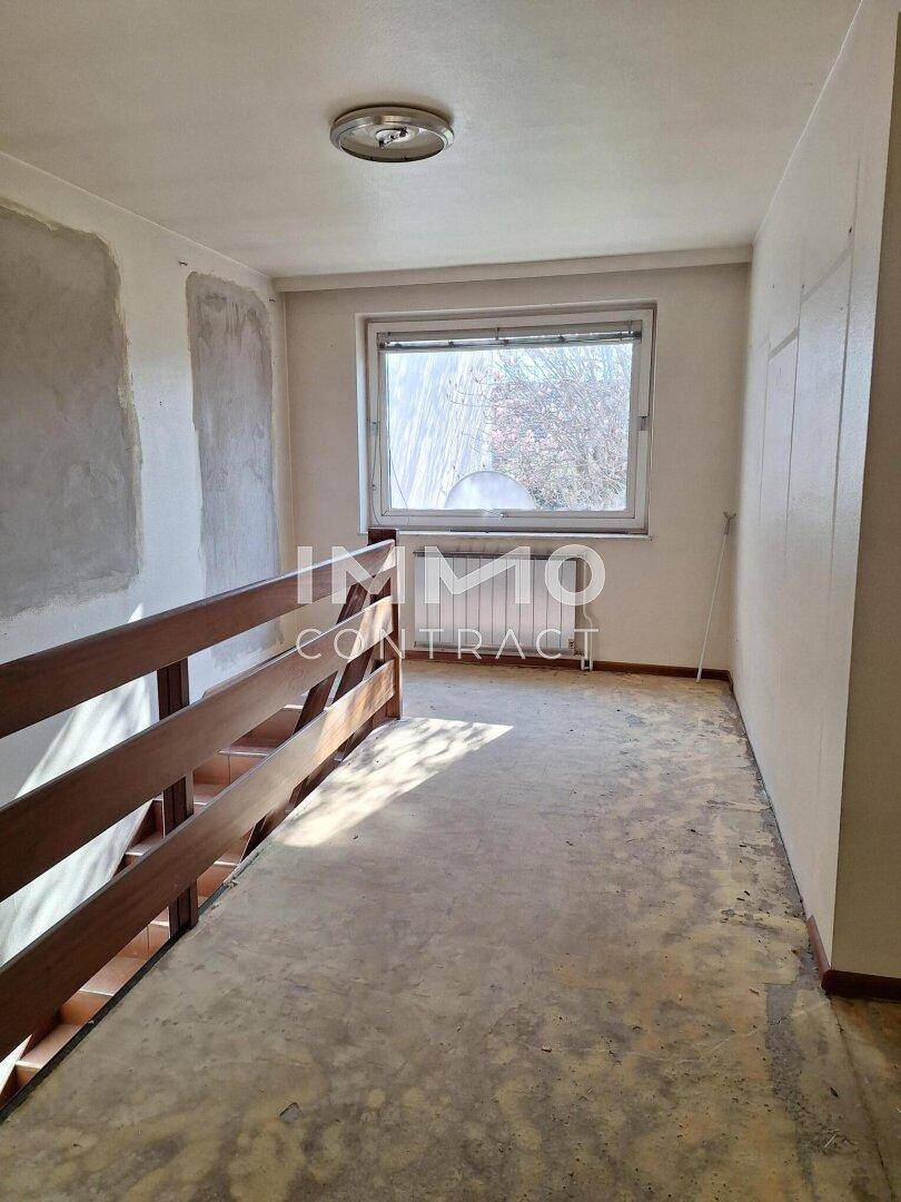 Oberer Flurbereich mit Fenster und Holzgeländer, bietet natürliches Licht und Renovierungspotenzial.