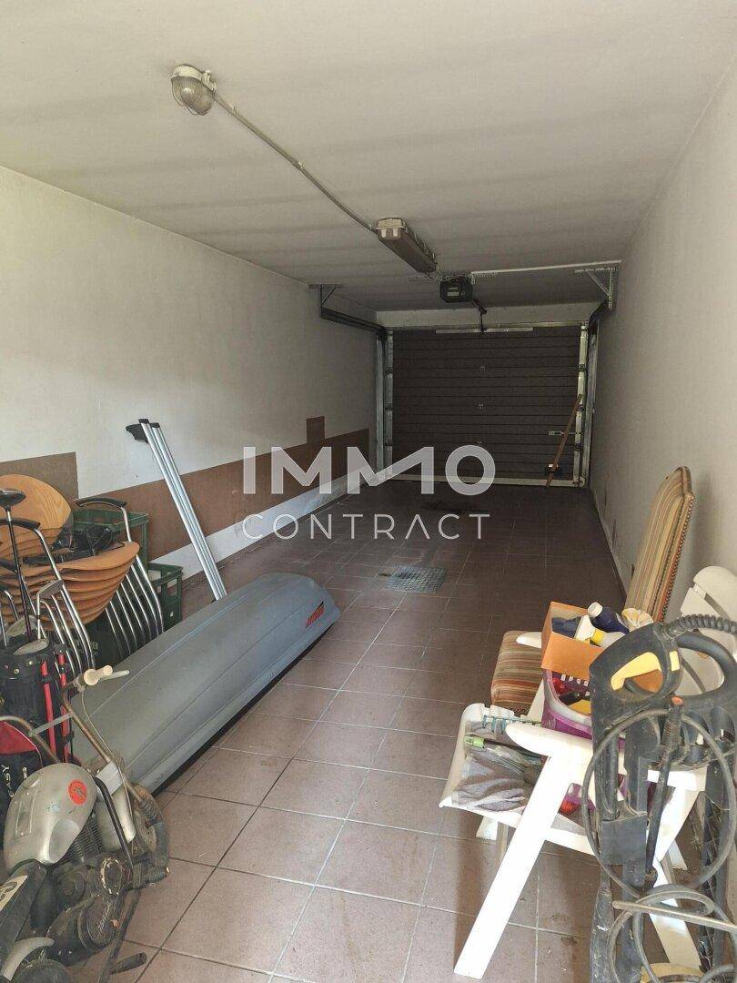 Geräumige Garage mit Fliesenboden, Rolltor und Abstellmöglichkeiten für diverse Gegenstände.