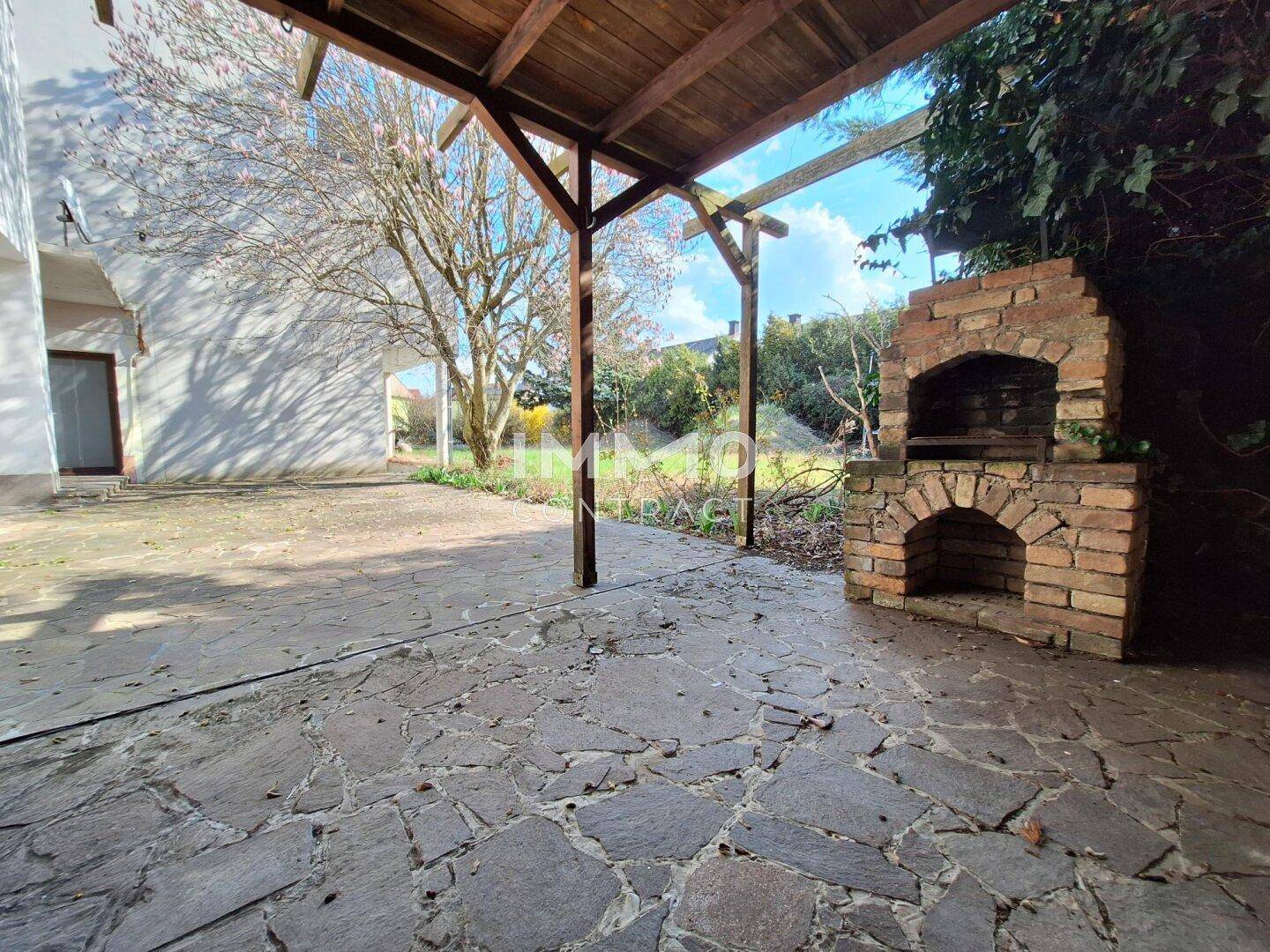 Große gepflasterte Terrasse mit Holzpergola und gemauertem Grill im Gartenbereich.