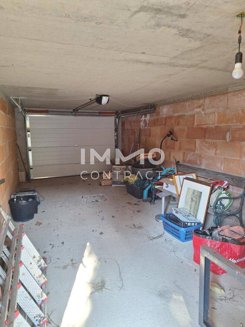 Unfertige Garage mit Betonboden, Rolltor und unverputzten Ziegelwänden.