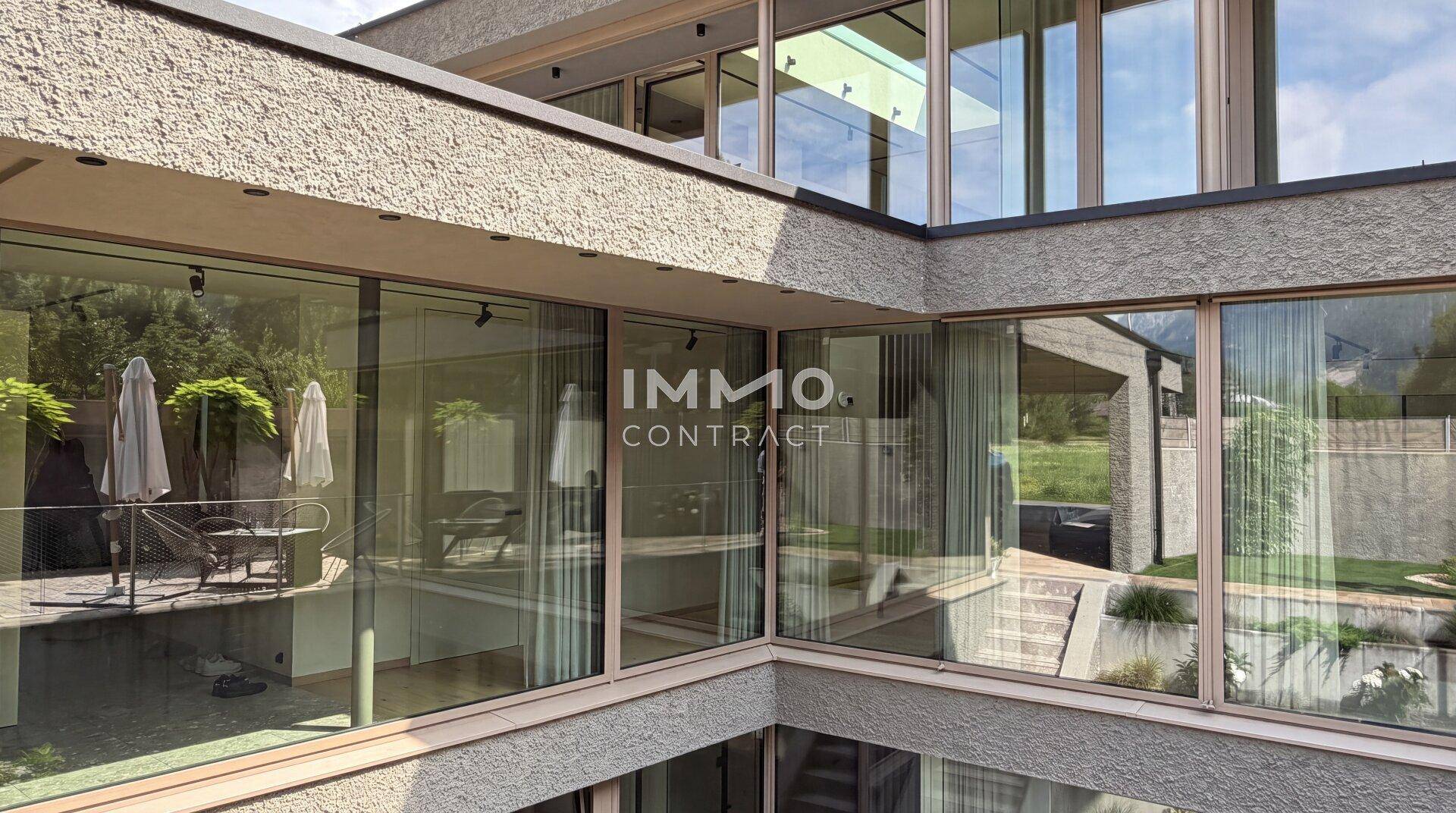Moderne Architektur mit weitläufiger Glasfassade und einer möblierten Terrasse mit Blick ins Grüne.