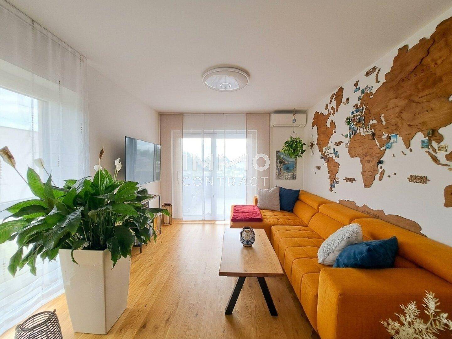 Helles Wohnzimmer mit großem orangefarbenem Sofa, Holzboden und Blick nach draußen.