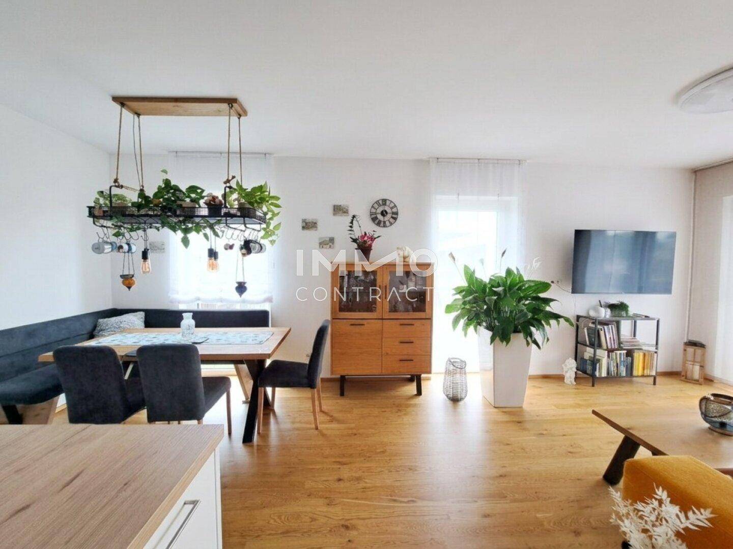Offener Wohn- und Essbereich mit Holzboden, großem Esstisch und gemütlichem Sofa.