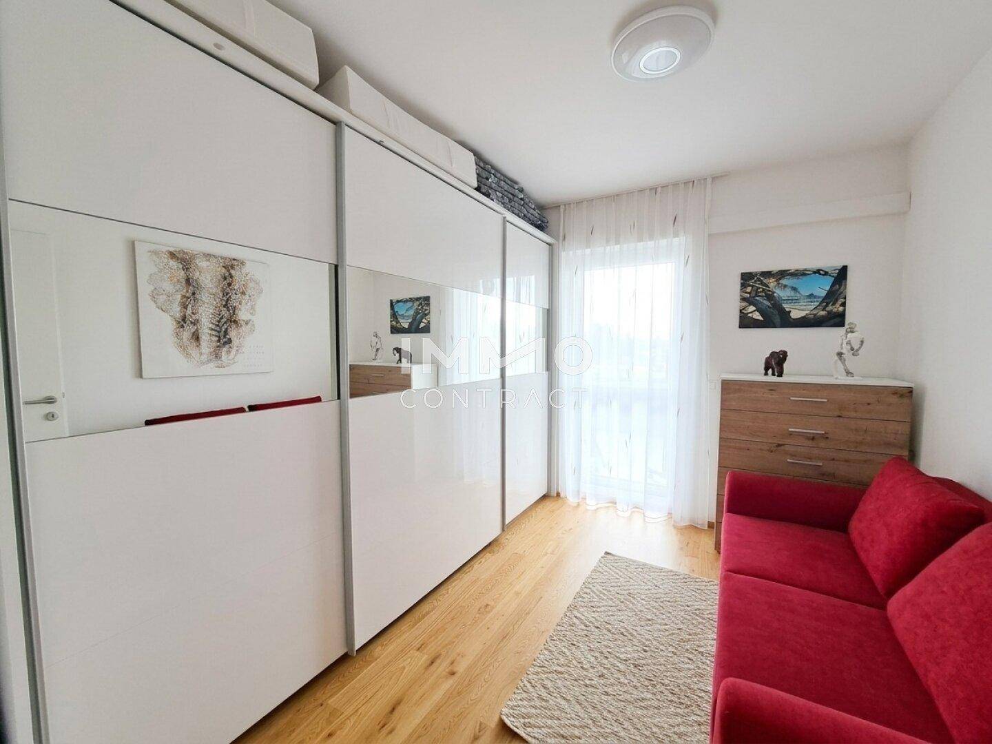 Helles Schlafzimmer mit rotem Sofa, großem Spiegelschrank und Holzboden.