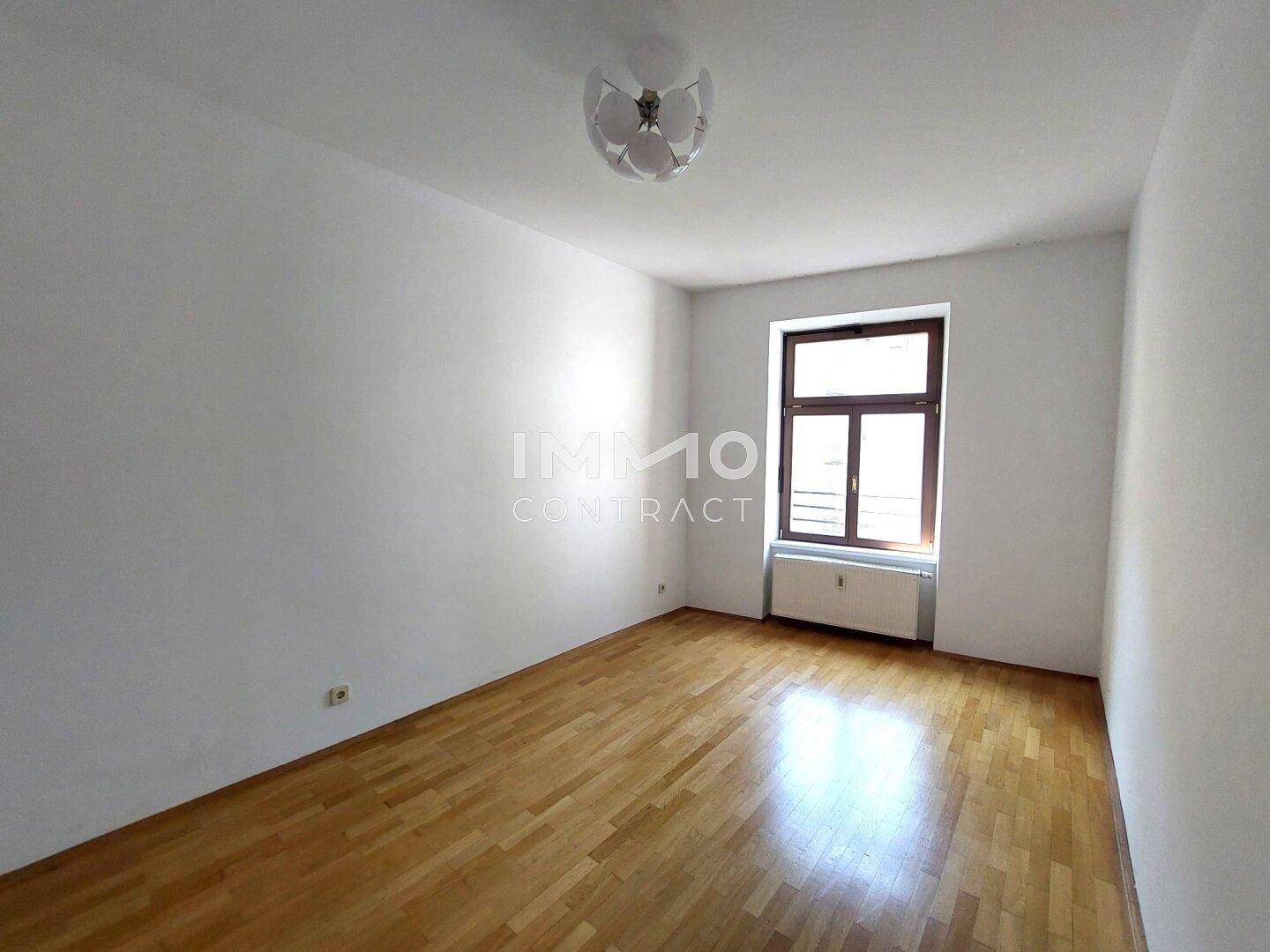 Gemütliches Schlafzimmer mit Parkettboden, weißen Wänden und einem Fenster.