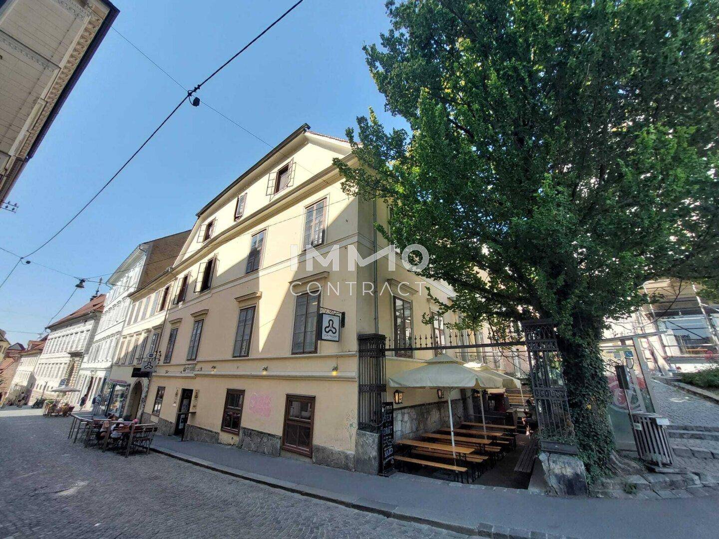 Historisches Gebäude mit gelber Fassade und Außengastronomie an einer belebten Straße.
