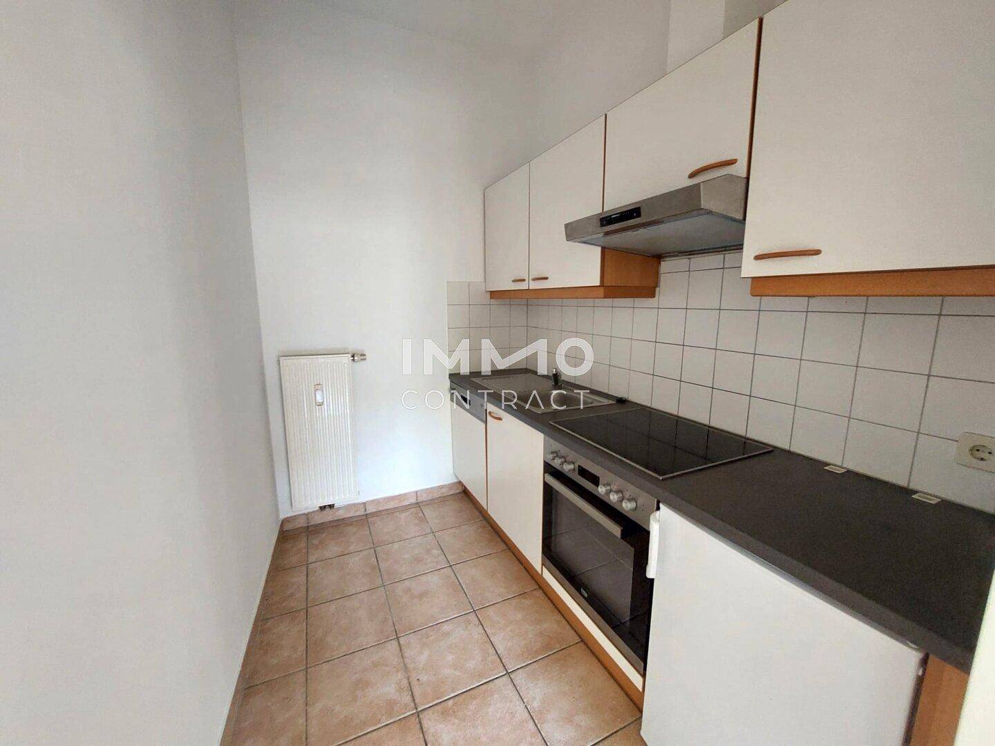 Kleine Küche mit weißen Schränken, dunkler Arbeitsplatte und Fliesenboden.