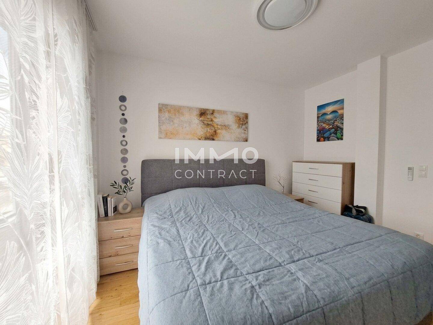Helles Schlafzimmer mit Doppelbett, Holzboden und Fenster mit Vorhängen.