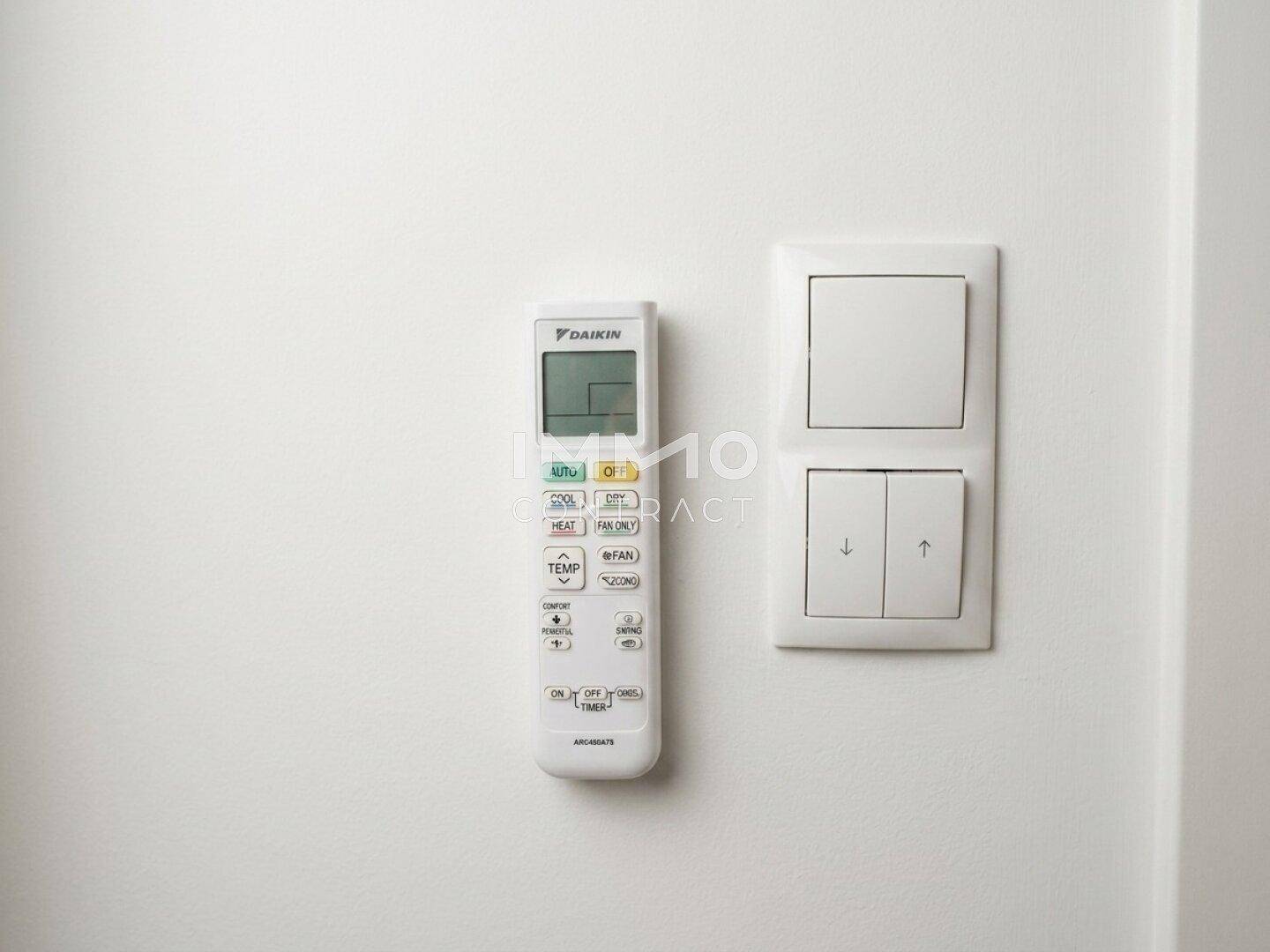 Fernbedienung der Klimaanlage und Lichtschalter an einer weißen Wand.