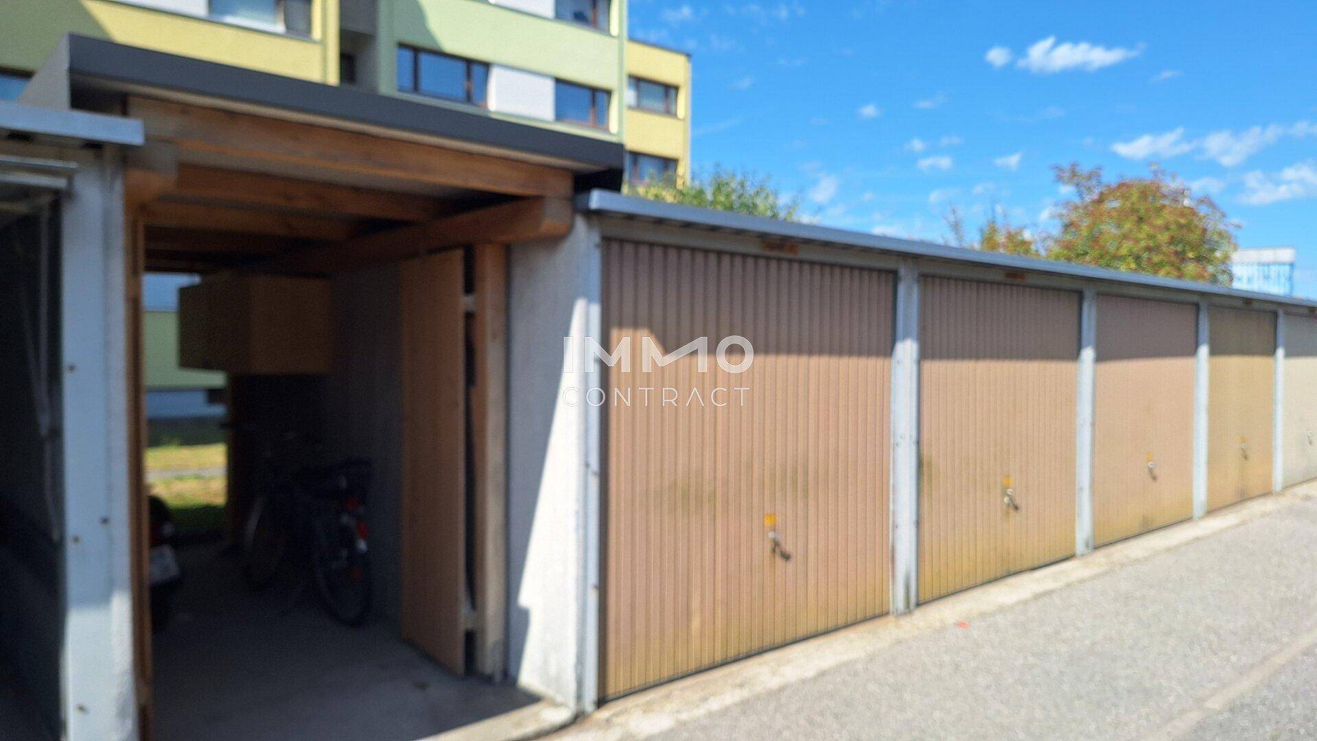 Reihe von Garagen mit Holztoren und einem überdachten Carport-Bereich.