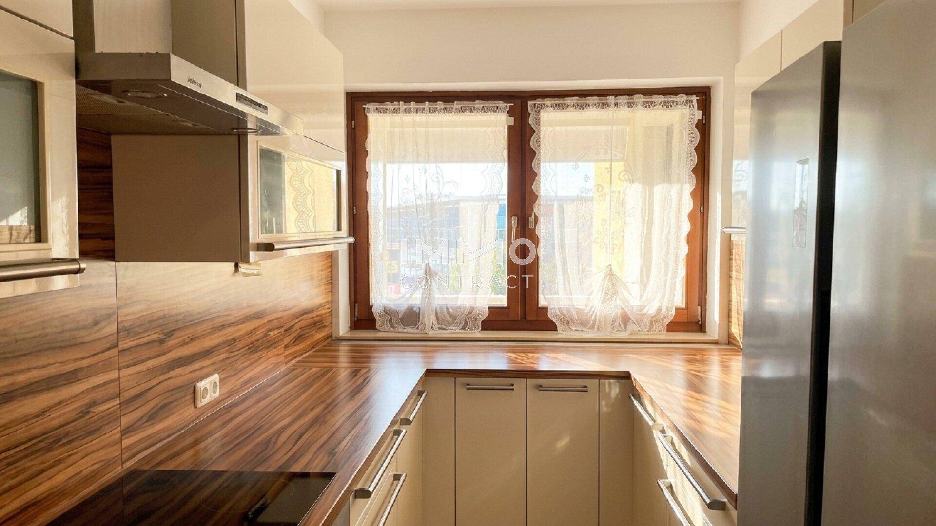 Helle Küche mit Holzoptik-Arbeitsplatten, weißen Schränken und Fensterblick.