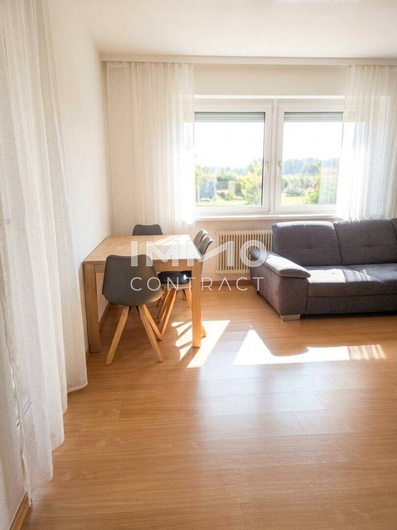 Heller Wohn- und Essbereich mit Holzboden, Sofa und großem Fenster.
