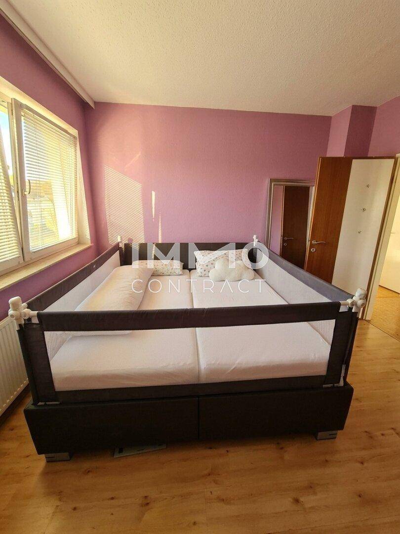 Schlafzimmer mit lila Wänden, Doppelbett und Holzboden, hell und freundlich.