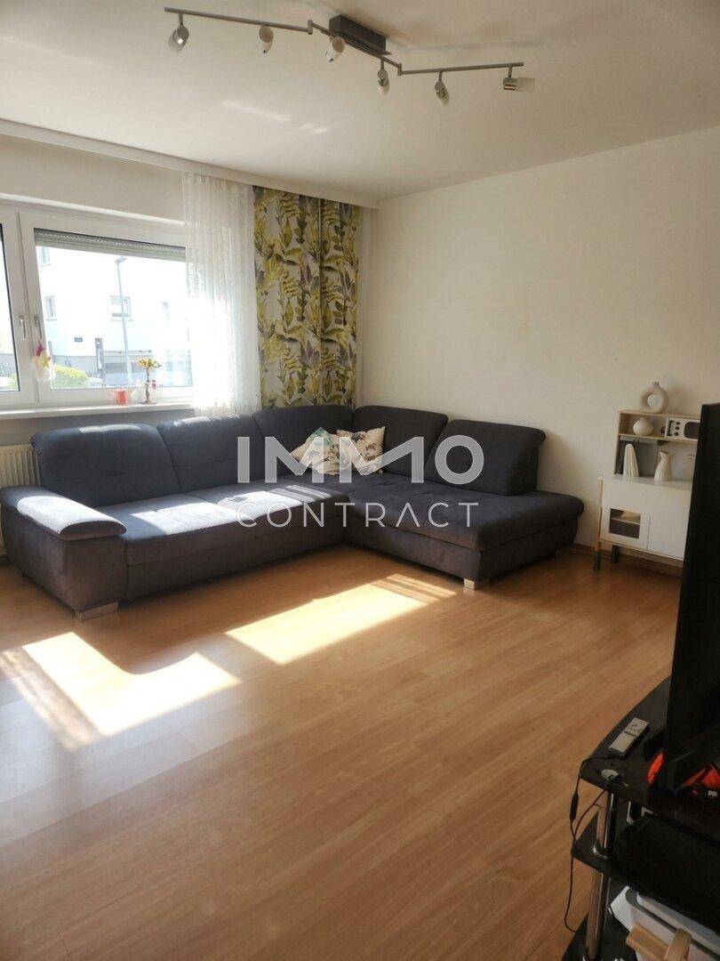 Gemütliches Wohnzimmer mit großem Ecksofa, Holzboden und hellem Fenster.