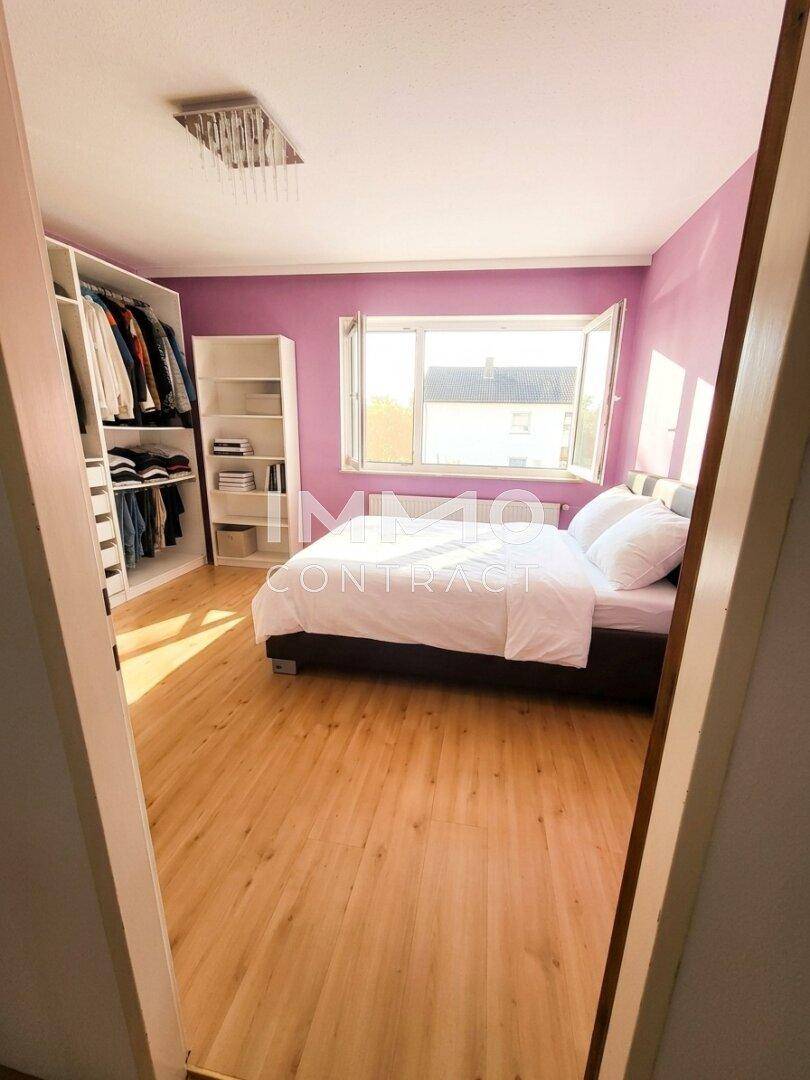 Schlafzimmer mit lila Wänden, Doppelbett und offenem Kleiderschrank-System.
