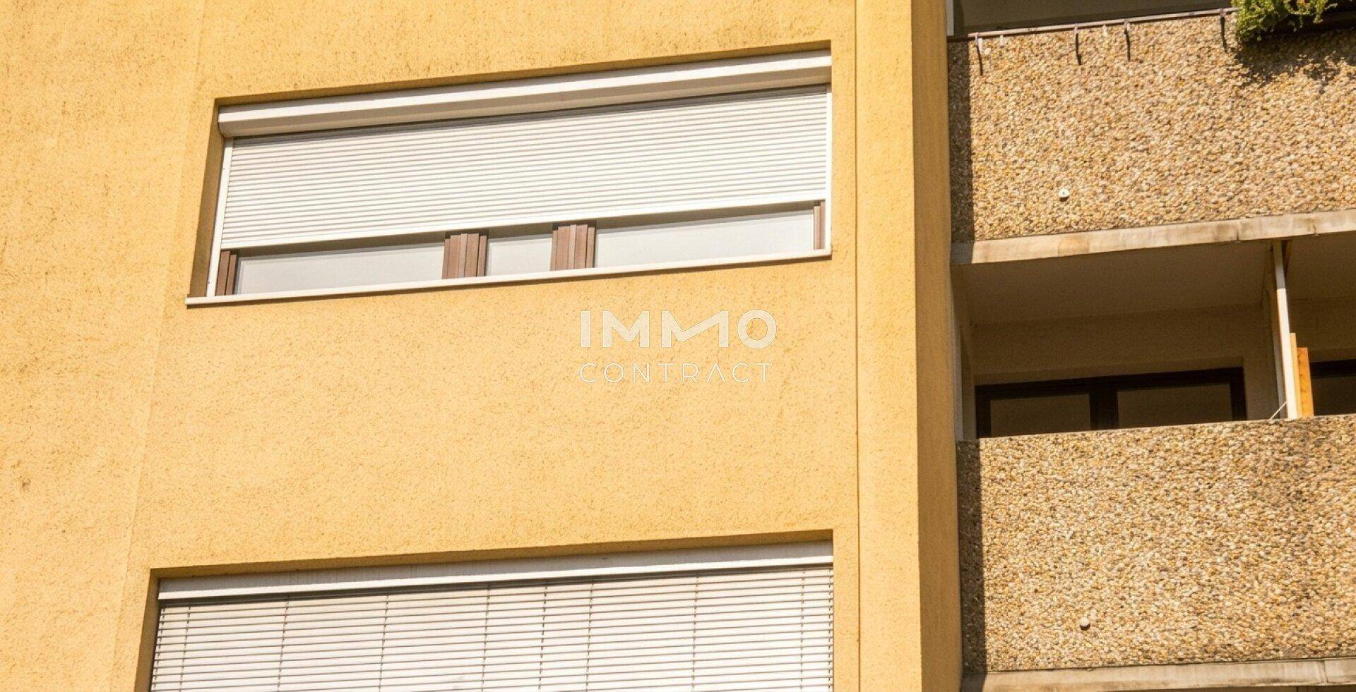 Fenster mit geschlossenen Rollläden an der gelben Fassade des Gebäudes.