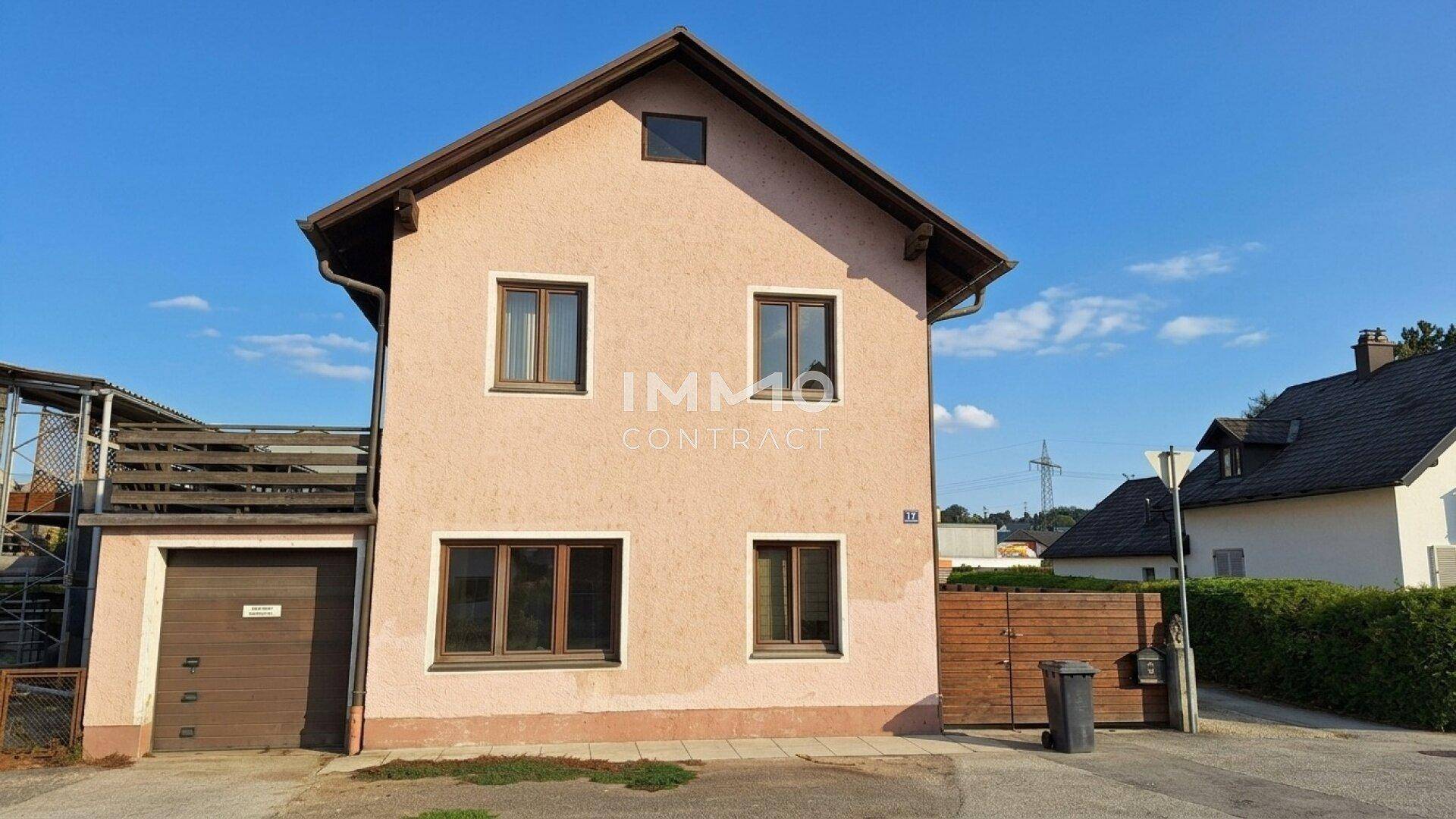 Vorderansicht des Hauses mit Garage und rosafarbener Fassade unter blauem Himmel.
