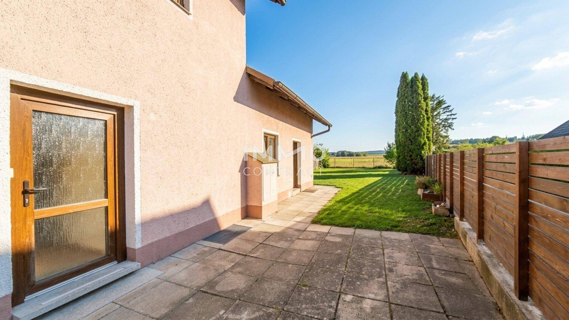 Seitenbereich des Hauses mit gepflasterter Terrasse und angrenzendem Rasen.