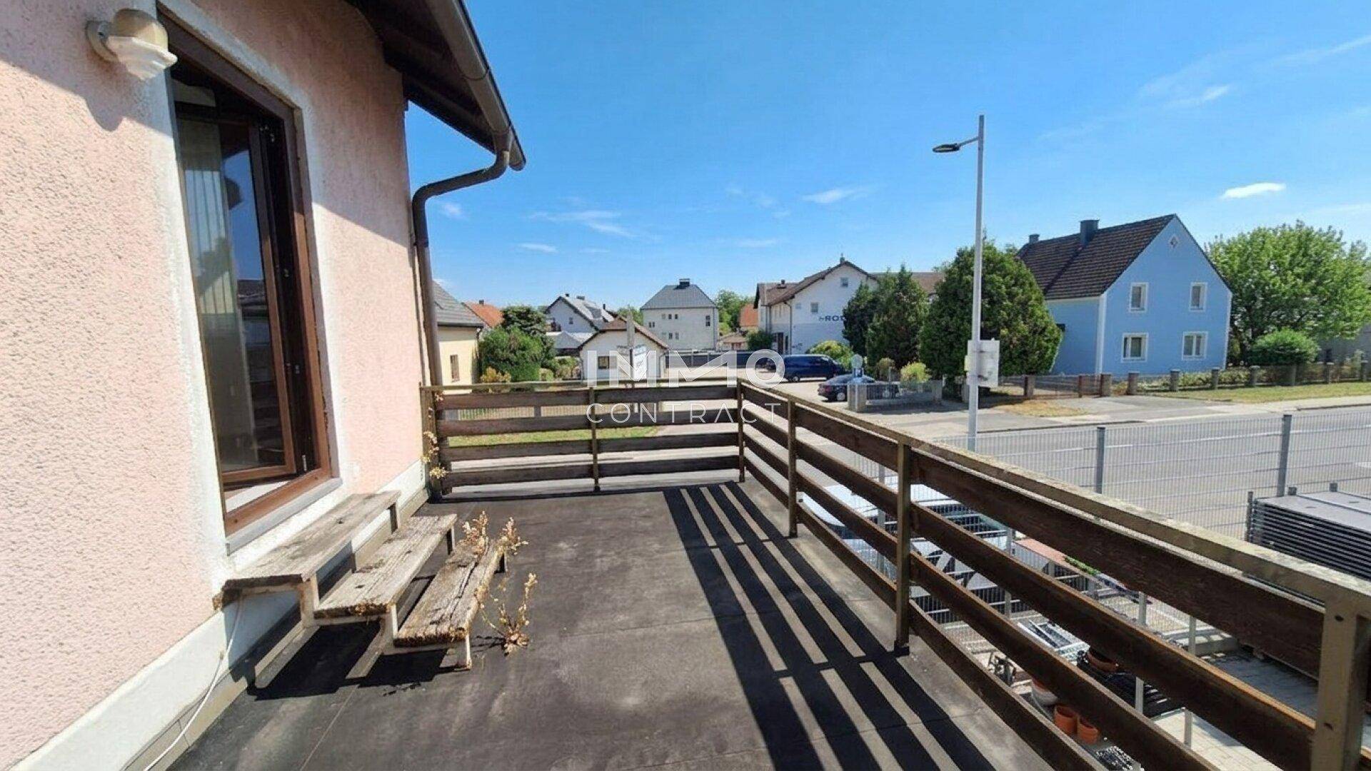 Kleiner Balkon mit Holzgeländer und Blick auf die Nachbarschaft und Straße.