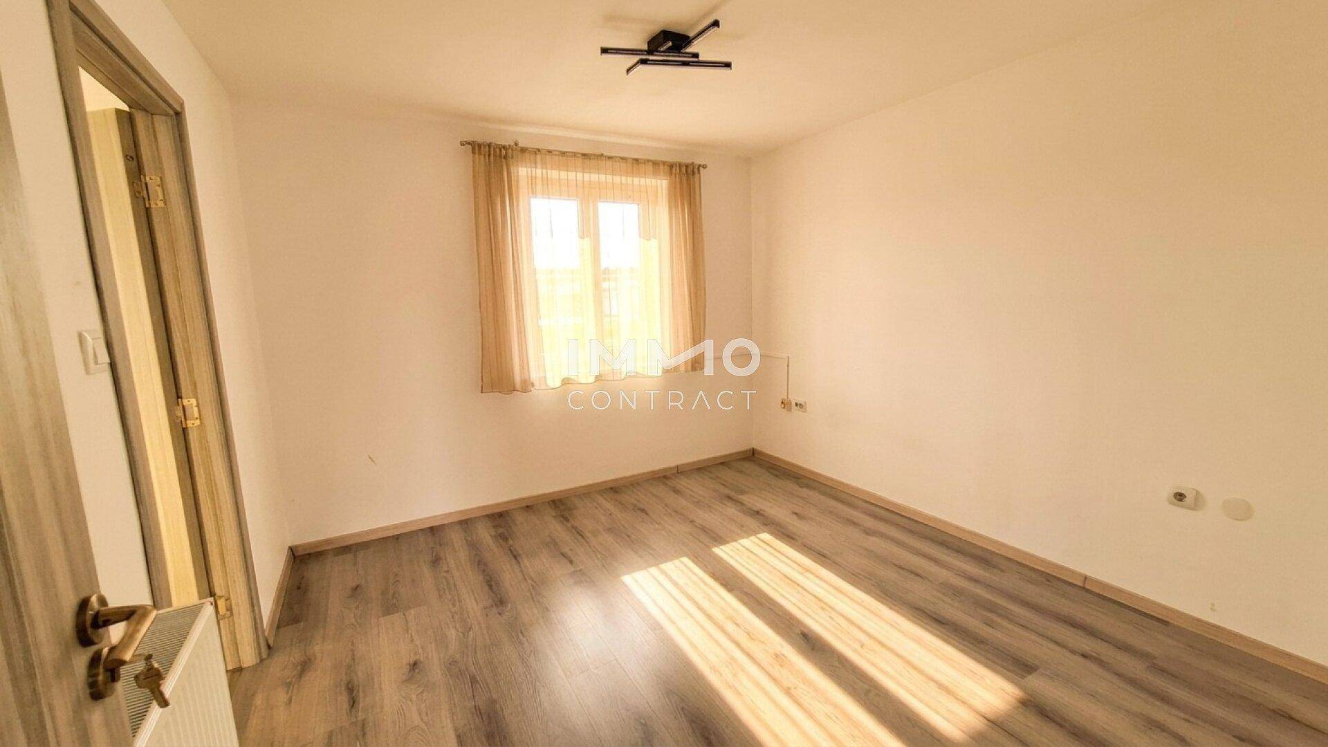 Gemütliches Schlafzimmer mit Laminatboden und Vorhängen am Fenster.