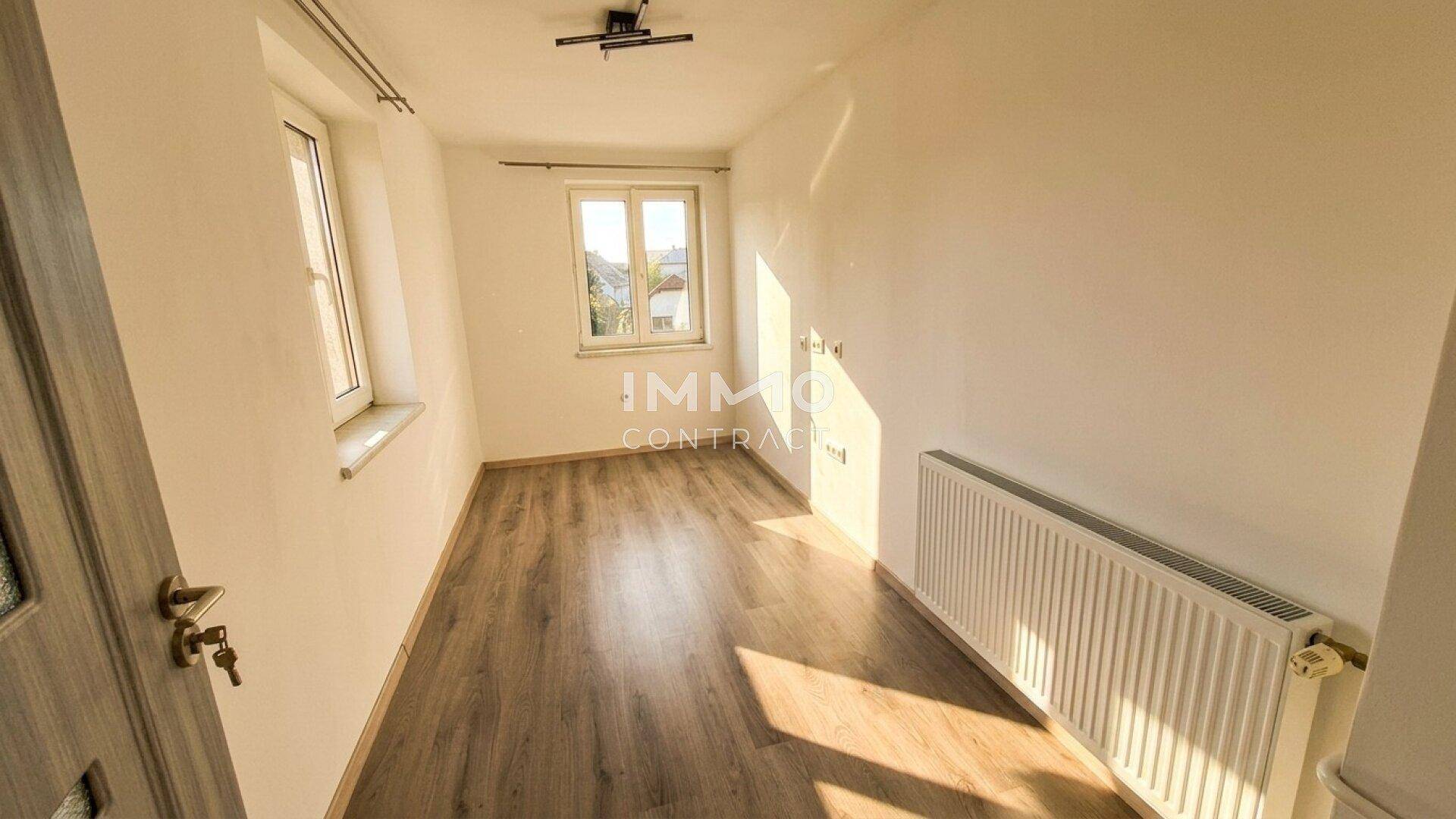 Helles Schlafzimmer mit Laminatboden und einem Fenster, das die Morgensonne einfängt.