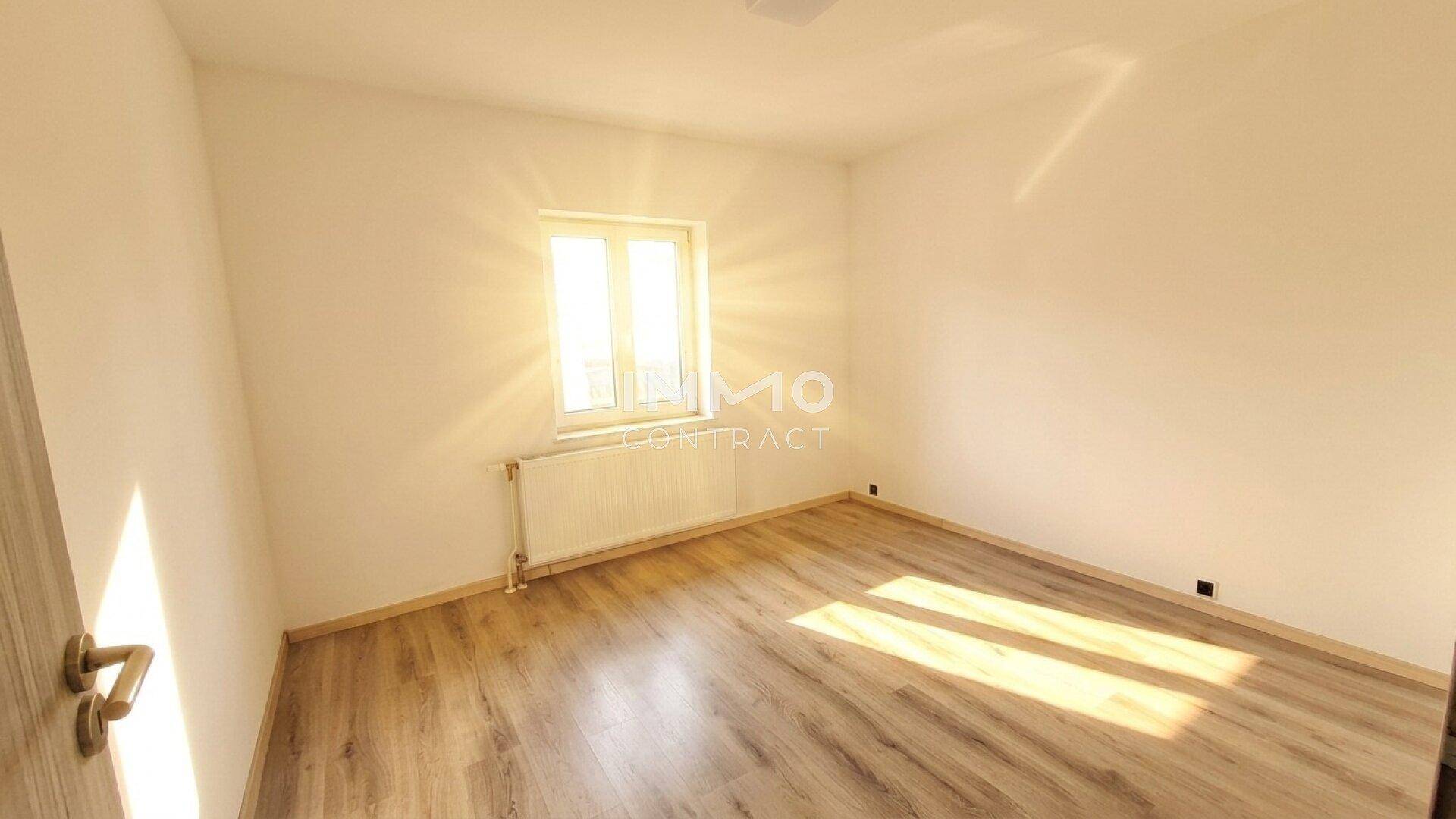 Sonniges Schlafzimmer mit Laminatboden und einem Fenster, das viel Licht hereinlässt.