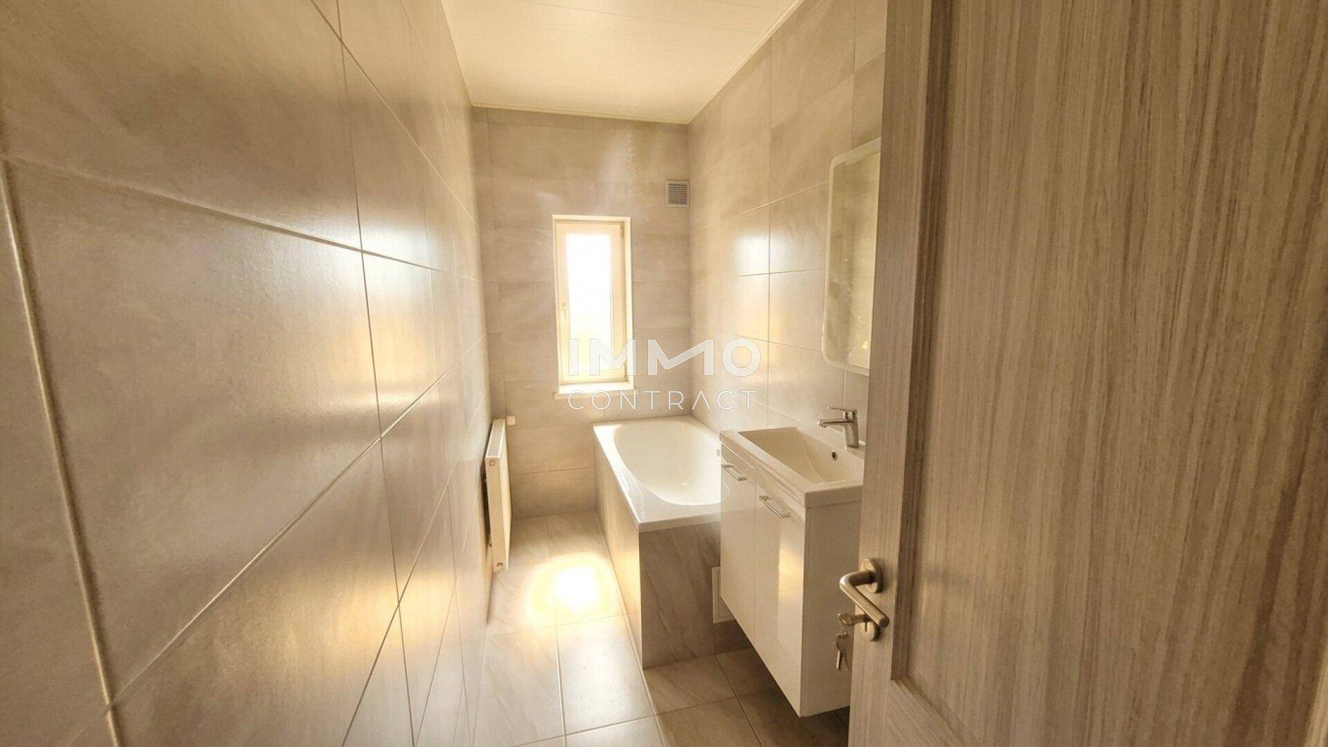 Gefliestes Badezimmer mit Badewanne, Waschbecken und kleinem Fenster.