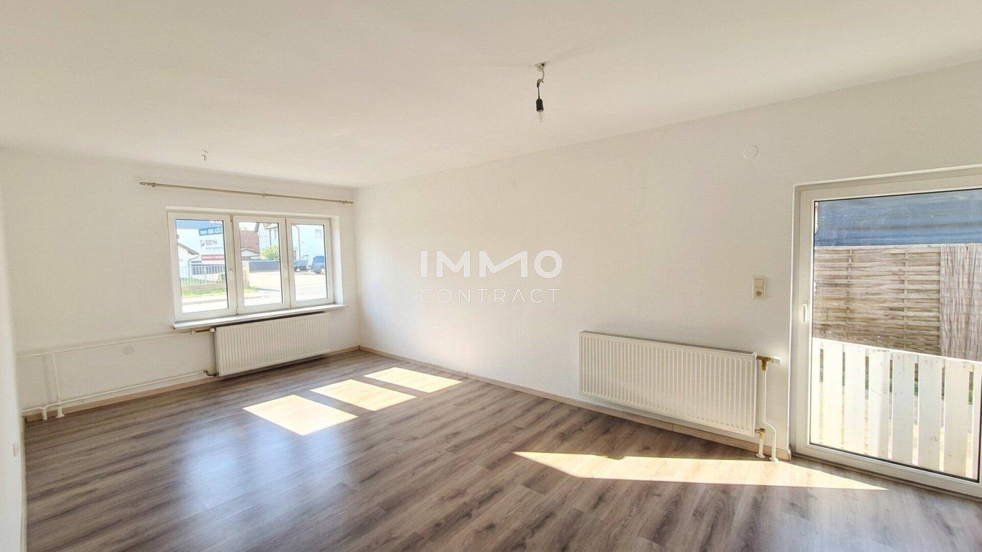Helles Wohnzimmer mit Laminatboden, großen Fenstern und Heizkörpern.