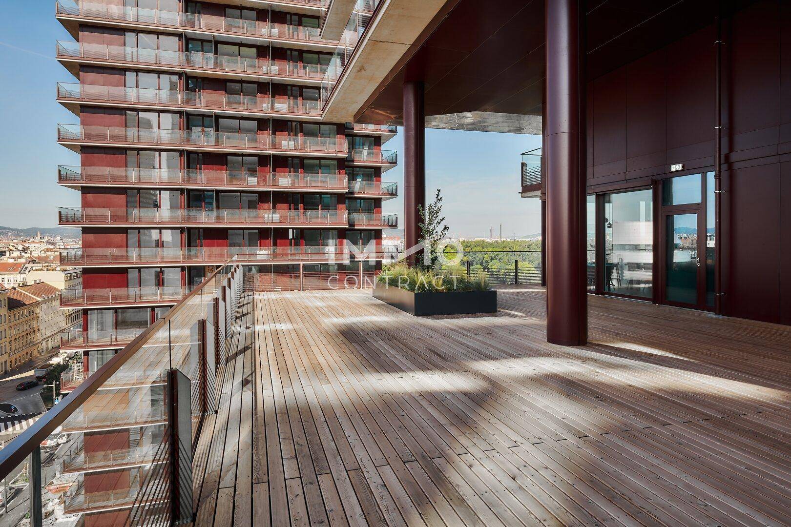 Geräumige Terrasse mit Holzboden und Glasgeländer, bietet einen weiten Blick über die Stadt.