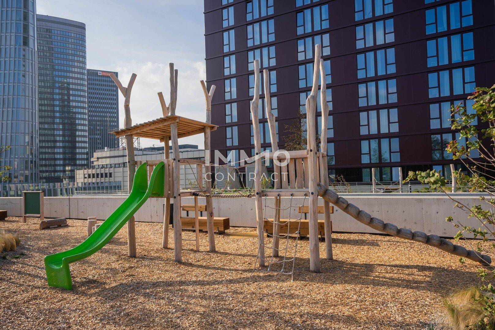 Moderner Spielplatz mit Rutsche und Klettergerüst, umgeben von zeitgenössischen Wohngebäuden.
