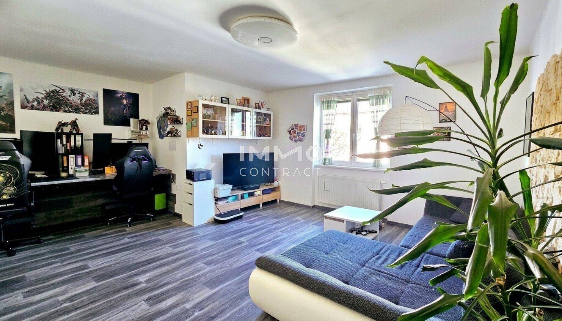 Geräumiges Wohnzimmer mit modernem Laminatboden, gemütlichem Sofa und einem Arbeitsbereich.