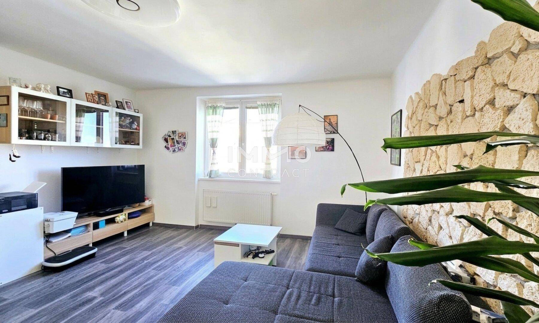 Helles Wohnzimmer mit einer dekorativen Steinwand, bequemer Couch und modernem Laminatboden.
