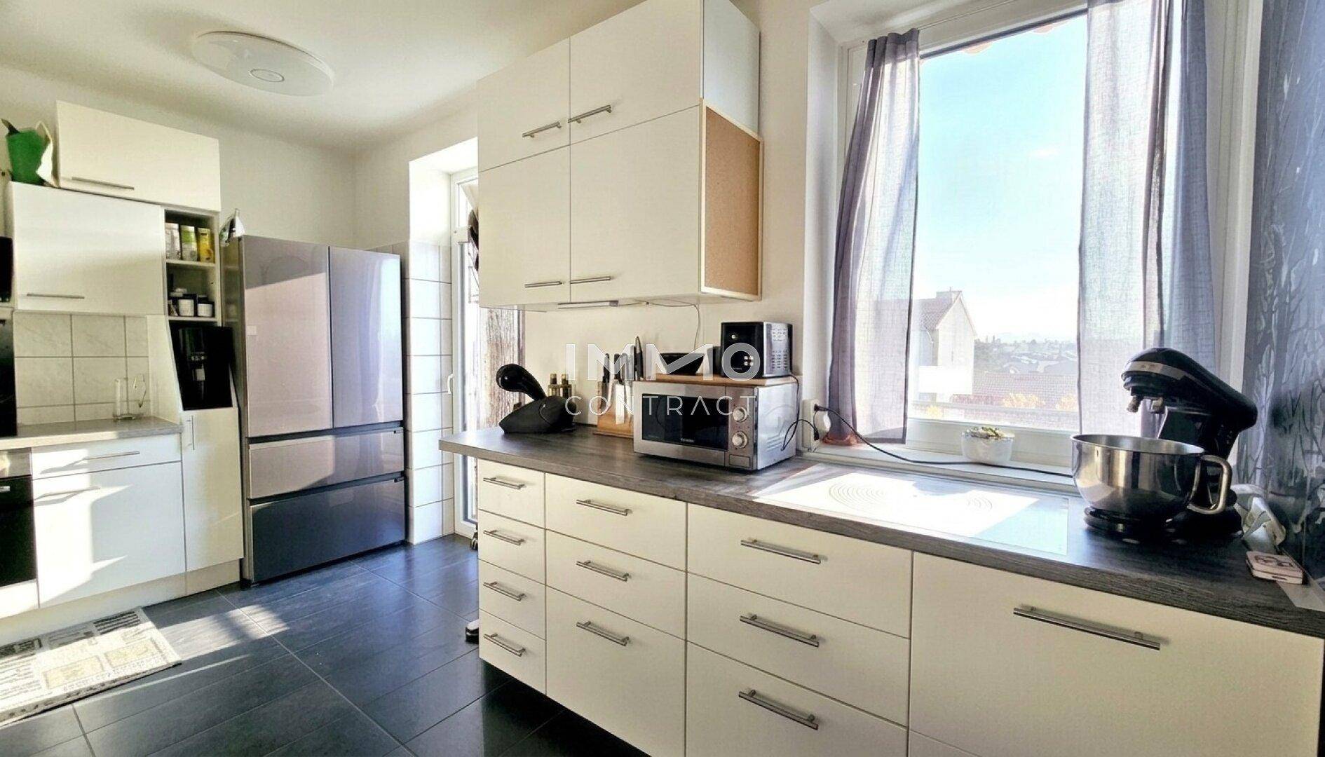 Helle Küche mit weißen Schränken, modernen Geräten und einem Fenster mit Ausblick.
