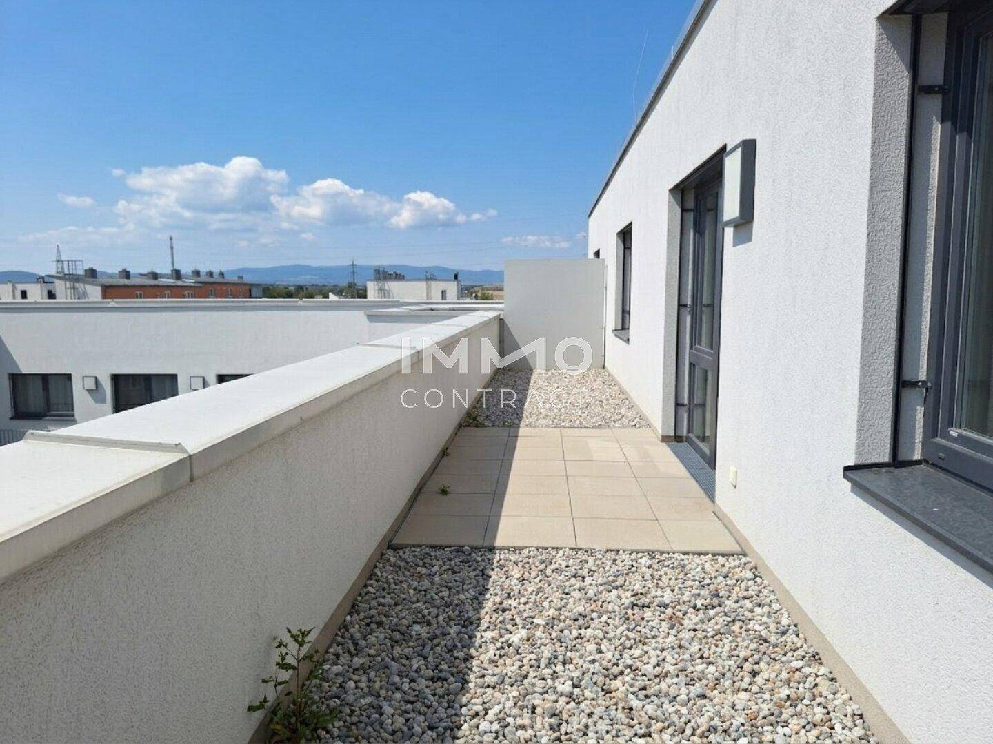 Lange, schmale Terrasse mit Kies und Fliesen, umgeben von weißen Mauern.