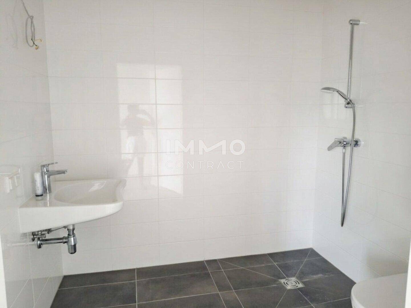 Modernes Badezimmer mit weißen Fliesen, grauen Bodenfliesen und einer Dusche.