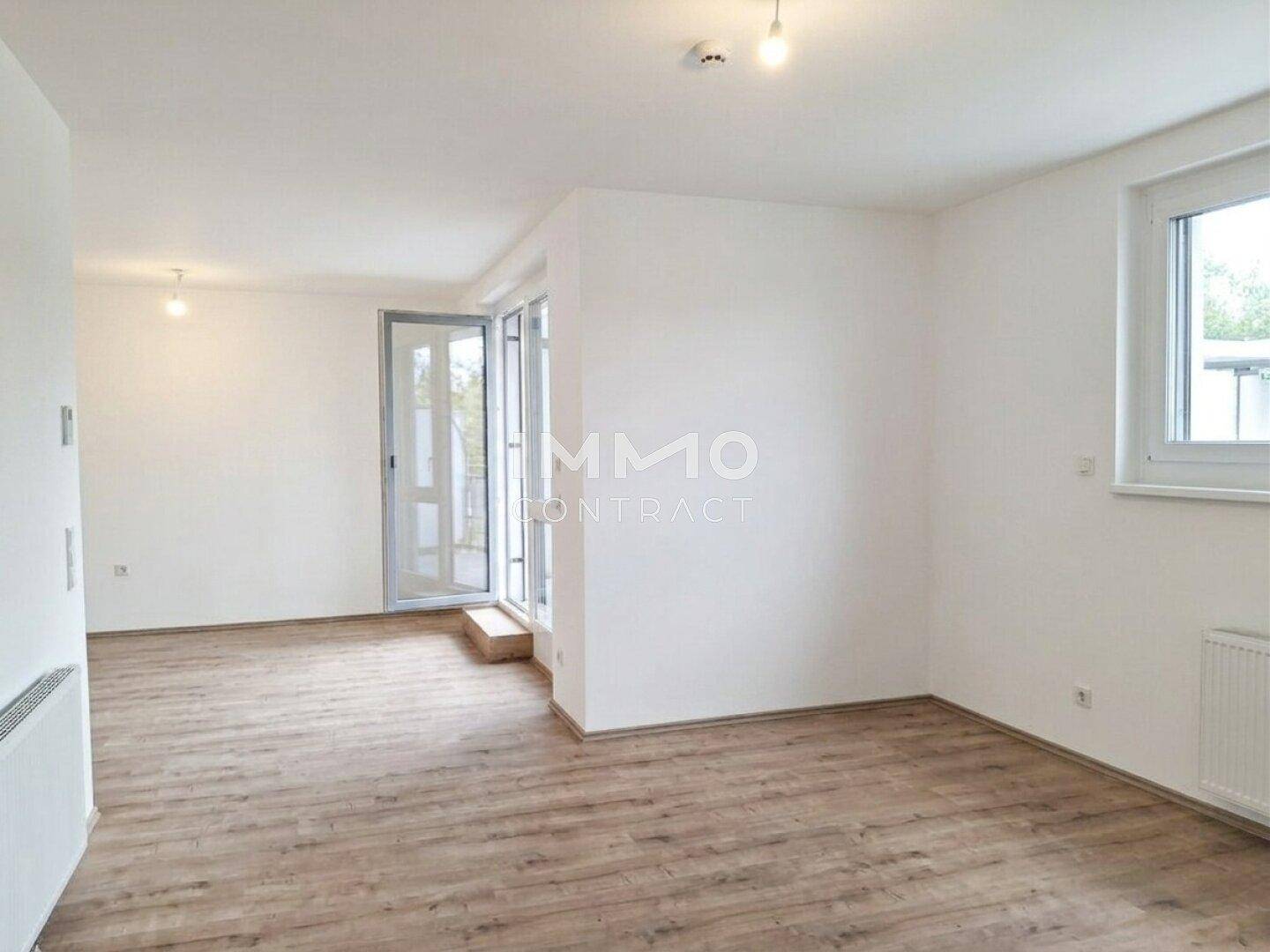 Heller Wohnbereich mit Laminatboden und Zugang zu einem Außenbereich durch eine Glastür.