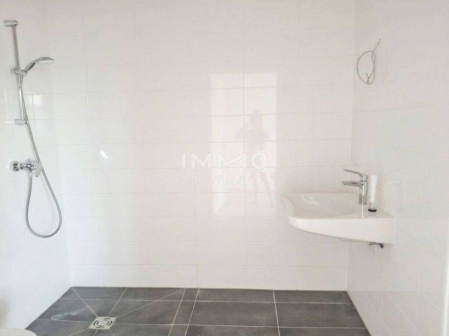 Modernes Badezimmer mit weißen Fliesen, ebenerdiger Dusche und einem einzelnen Waschbecken.