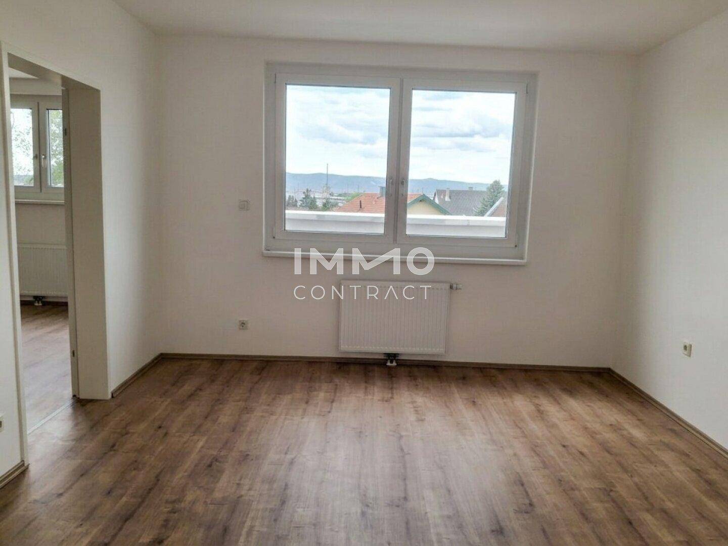 Leeres Zimmer mit Laminatboden und großem Fenster mit Blick ins Grüne.