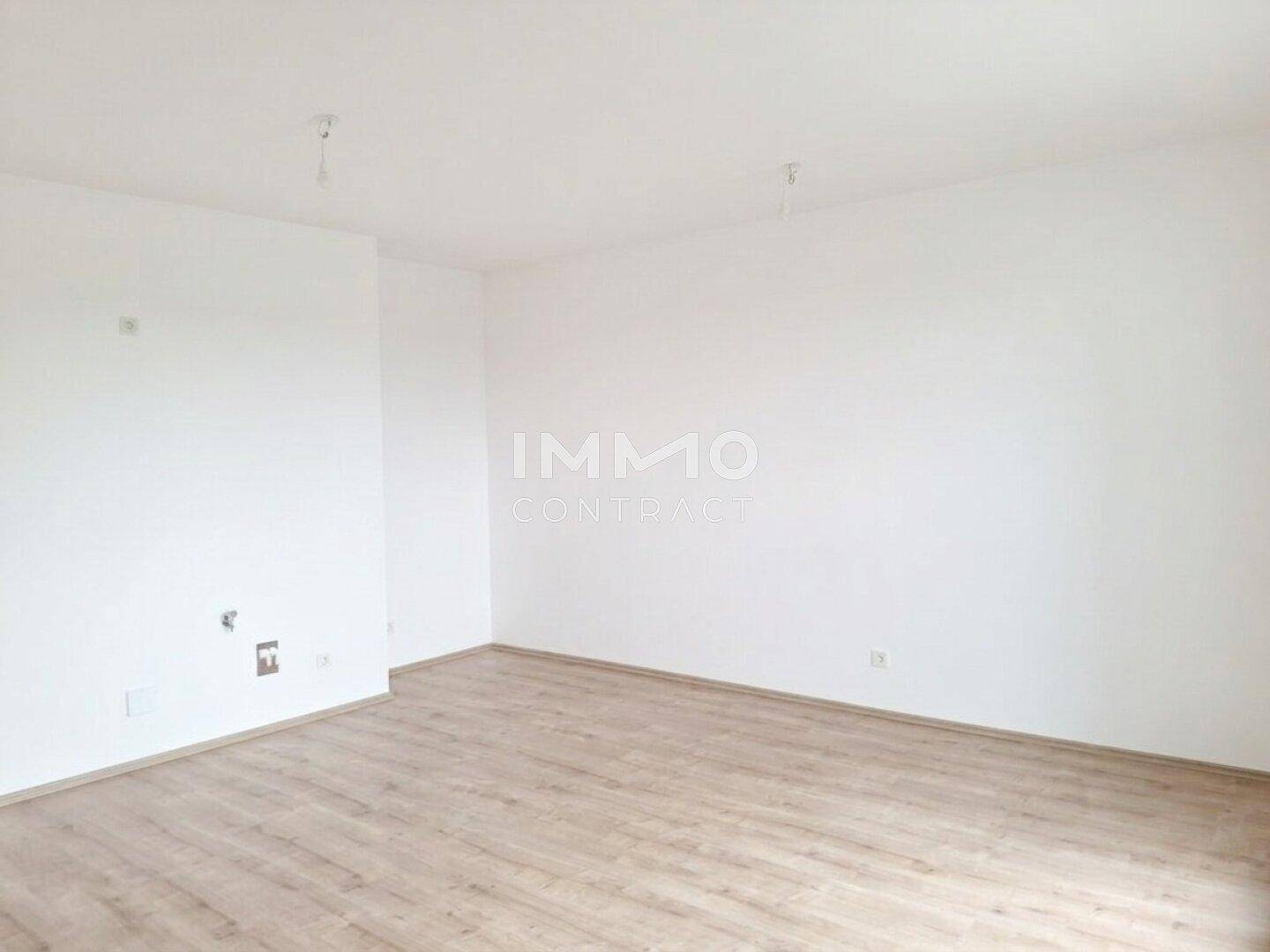 Geräumiges, leeres Zimmer mit Laminatboden und weißen Wänden.