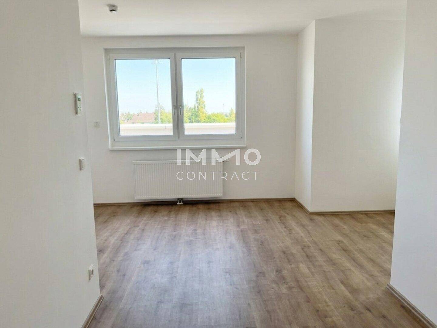 Freundlicher Wohnraum mit großem Fenster, Heizkörper und Blick ins Grüne.