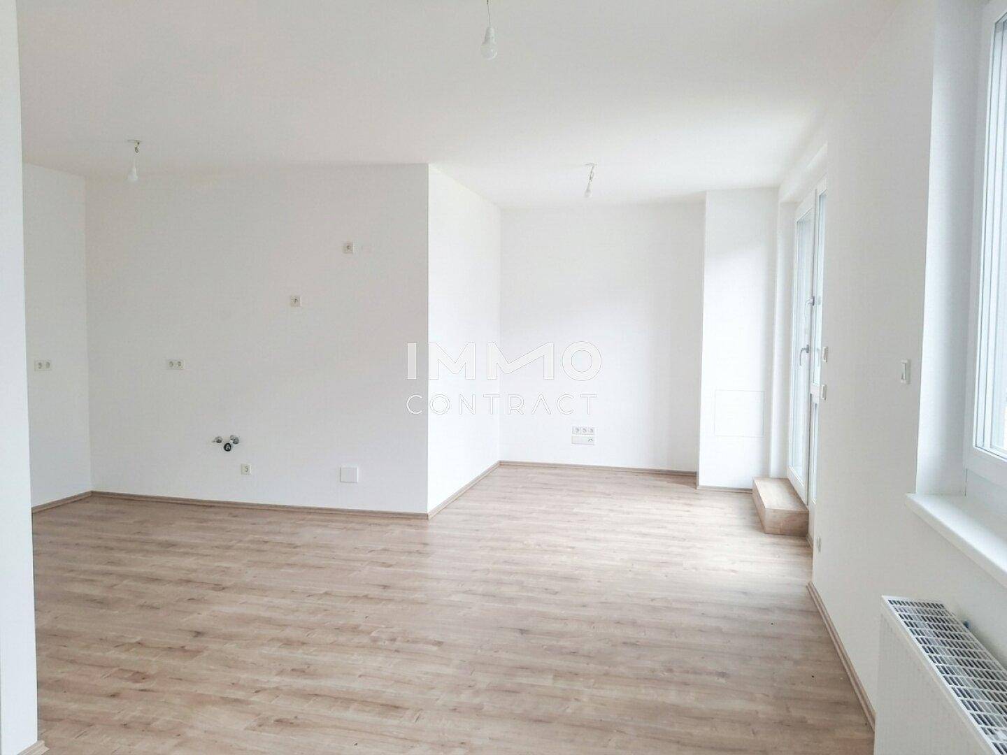Geräumiger, heller Wohnbereich mit Laminatboden und Zugang zu einem Außenbereich.