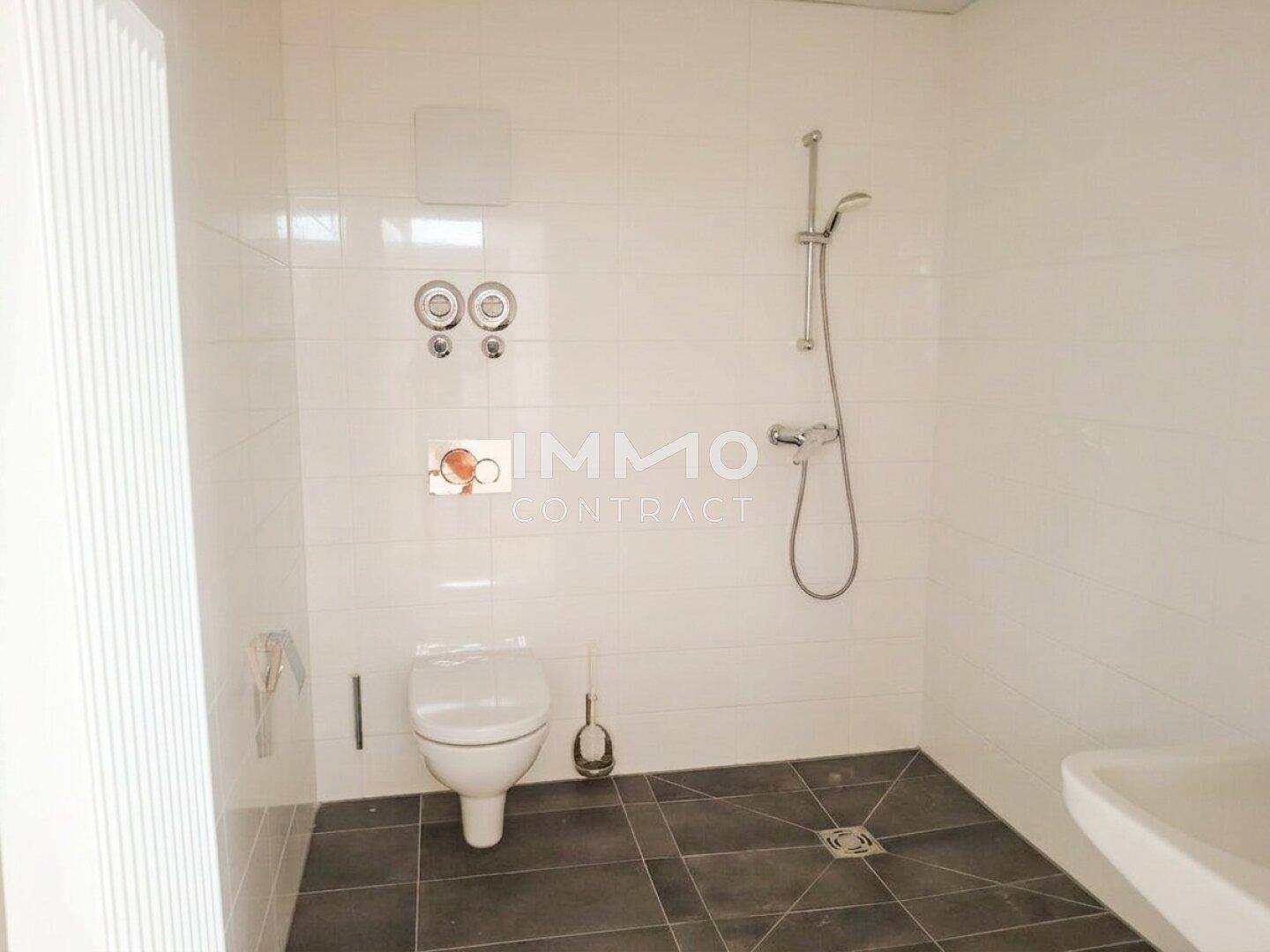 Modernes Badezimmer mit Dusche, WC und Waschbecken, ausgestattet mit hellen Wand- und dunklen Bodenfliesen.
