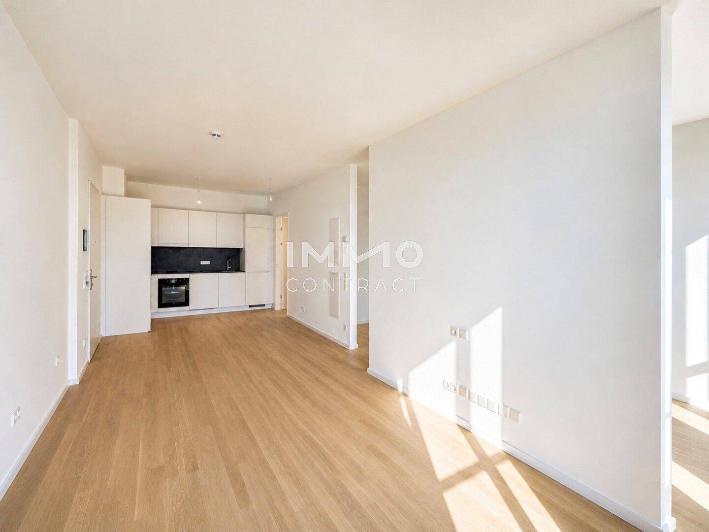 Heller Wohnbereich mit Holzboden und integrierter, moderner Küchenzeile im Hintergrund.